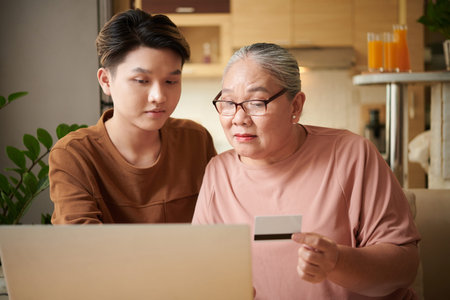 Teenage boy showing grandmother how to pay utility bills online with credit cardの写真素材