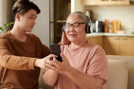Teenage boy explaining grandmother how she can listening to music from playlist on smartphoneの写真素材