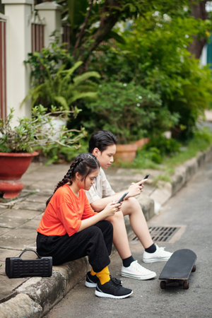 Teenagers sitting on pavement and texting or playing games on smartphonesの写真素材