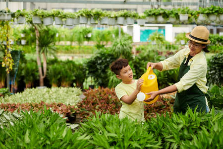 Mother showing son how to water plants at outdoors flower shopの写真素材