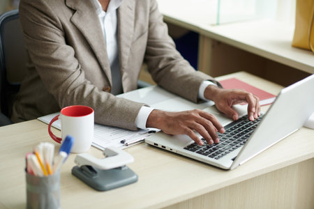 Cropped image of entrepreneur drinking coffee and working on laptop at office deskの写真素材