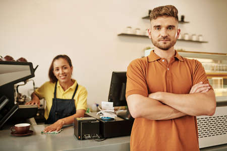 Positive coffeeshop owner standing at counter with arms crossedの写真素材