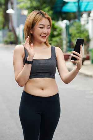 Portrait of happy young sportswoman video calling her fitness trainer after jogging outdoorsの写真素材