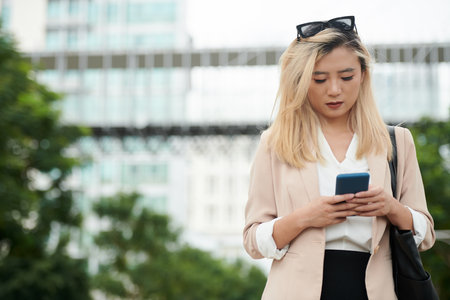 Young businesswoman checking notifications in smartphone when walking to office in ther morningの写真素材