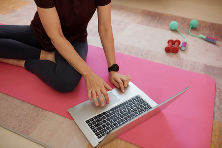 Young woman sitting on yoga mat and searching for video of favorite fitness bloggerの写真素材