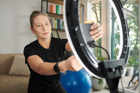 Fitness instructor setting filming equipment at home to record lesson for subscribers