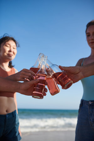 Group of friends clinking bottles of refreshing drink when enjoying beach party
