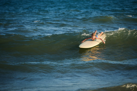 Preteen girl surfing in sea, catching waves and swimming