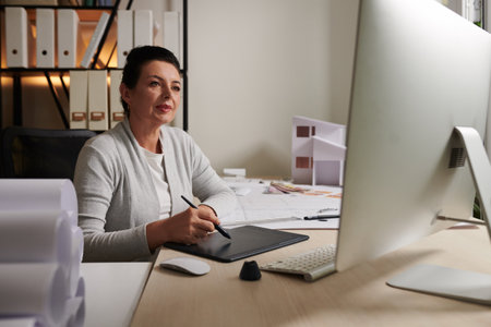 Mature female architect working on graphic tablet at her desk in bureauの写真素材