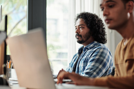 Pensive Indian programmer with curly hair looking at computer screen