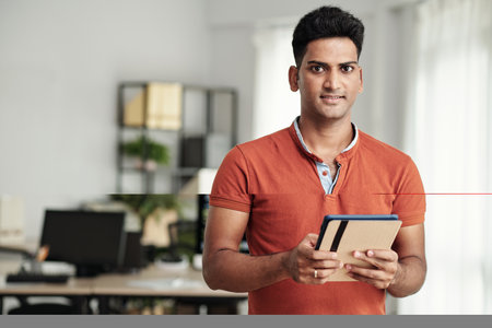 Portrait of smiling Indian software developer with digital tablet standing in officeの写真素材