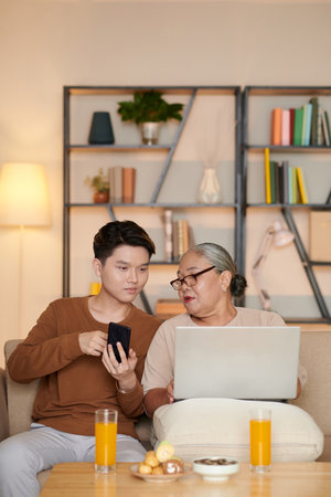 Teenage boy explaining grandmother how yo transfer images from smartphone to laptopの写真素材