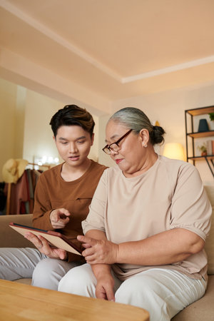 Senior woman asking teenage grandson help her with application on tablet computerの写真素材