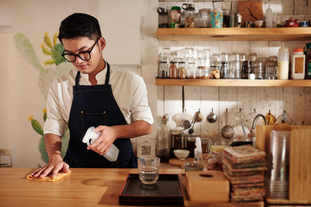 Coffeeshop barista wiping counter with disinfecting detergent