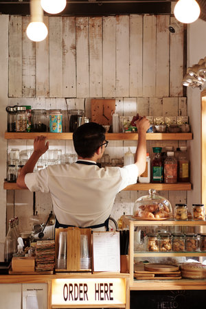 Cafe barista cleaning up shelves and refilling tea and coffee jars