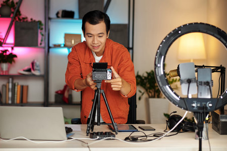 Horizontal medium portrait of modern Asian blogger getting ready for content recording adjusting camera on tripodの写真素材