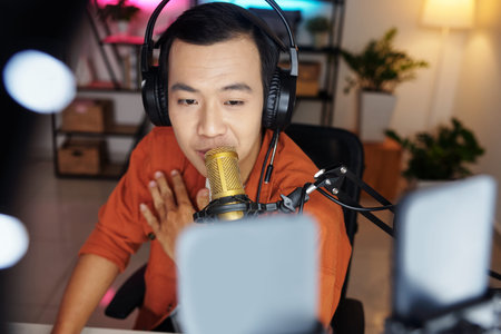 Selective focus high angle of modern young adult Asian influencer wearing headphones speaking on...