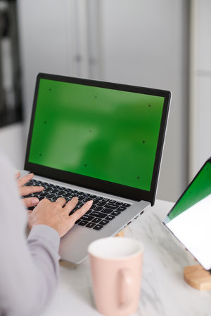 Hands of young female website designer working in front of green screen and pushing keys of laptop keypad while sitting by workplaceの写真素材