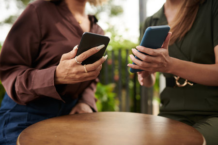 Close-up of two friends connecting with their mobile phones while sitting in cafeの写真素材