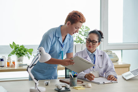 Young nurse consulting with doctor showing the patient card while they working at medical officeの写真素材
