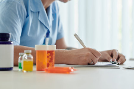Close-up of young nurse prescribing medicine for patient while sitting at table with bottles of...