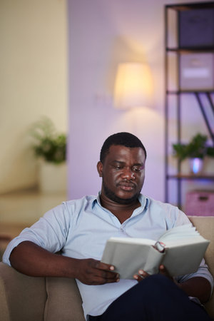 Portrait of serious Black man reading captivating book at home