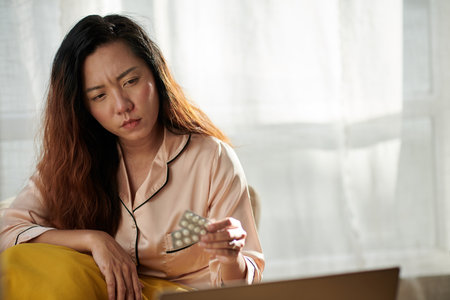 Portrait of sick woman suffering from fever looking at pile of prescribed medicineの写真素材