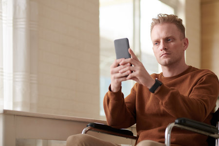 Portrait of serios young man with disability texting friendの写真素材