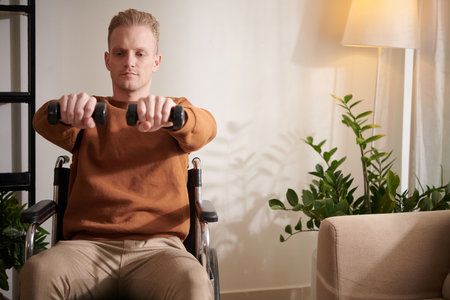 Young man with disability doing exercise with small dumbbells to train musclesの写真素材