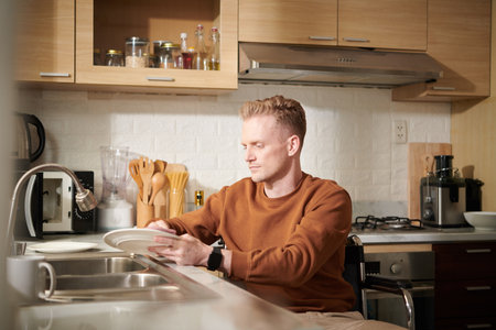 Young man with disability washing dishes in kitchen sinkの写真素材