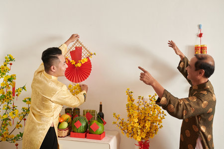 Happy senior man telling adult son whenre to hang Tet decoration on wallの写真素材