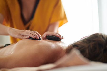Closeup image of woman massaging back of client with hot basalt stonesの写真素材