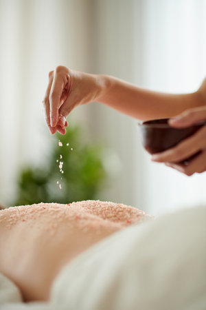 Closeup image of woman pinching infused salt scrub on back of female client of spa salonの写真素材