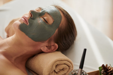 Woman with brightening clay mask on face relaxing on bed in spa salonの写真素材