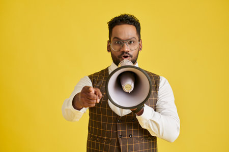 Man speaking in megaphone and pointing at camera, isolated on yellowの写真素材