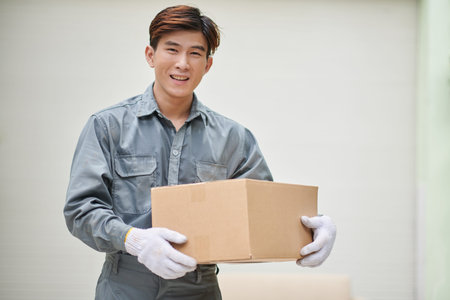 Smiling mover in grey uniform holding cardboard box