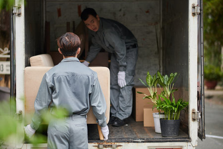 Movers loading furniture, cardboard boxes and potted plants in van