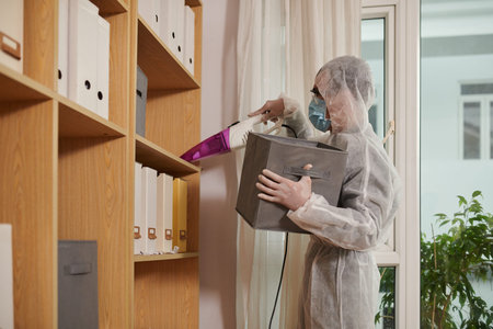 Desinfecting service worker vacuum cleaning shelves in office