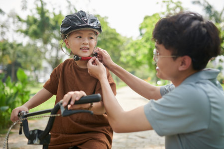 Father helping little boy to put on helmet before riding bicycleの写真素材