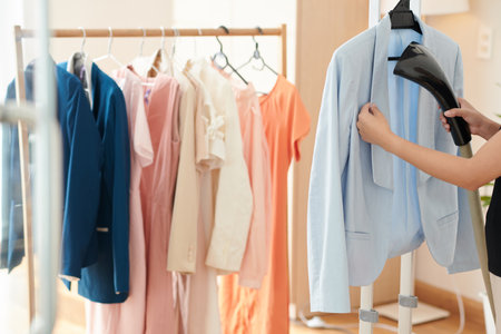 Woman steaming light blue jaket when getting ready for workの写真素材