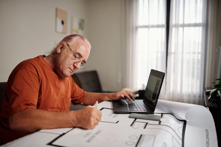 Senior man watching tutorial on laptop when drawing construction plan of his new house