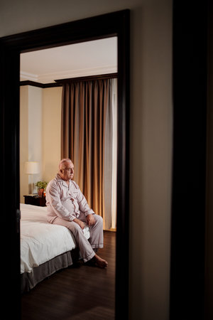 Unhappy elderly man sitting in bed at home after waking upの写真素材