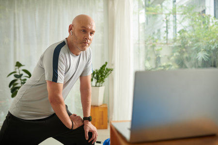 Mature man doing lunges when exercising at home with his online fitness instructorの写真素材