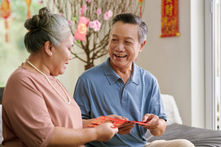 Joyful senior couple discussing lucky money envelopes they prepared for Tet celebrationの写真素材