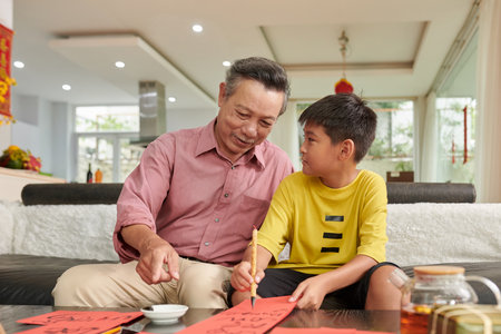 Senior man explaining teenage grandson how to use calligraphy brushの写真素材