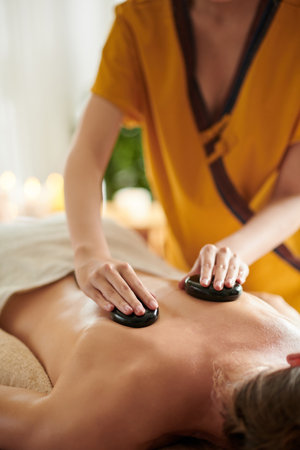 Cropped image of masseuse giving relaxing stone massage to female clientの写真素材