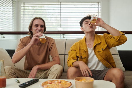 Young men drinking beer and eating pizza and snacks at homeの写真素材
