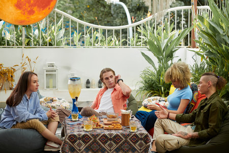 Group of friends gathered in outdoor cafe to have some food and discuss newsの写真素材