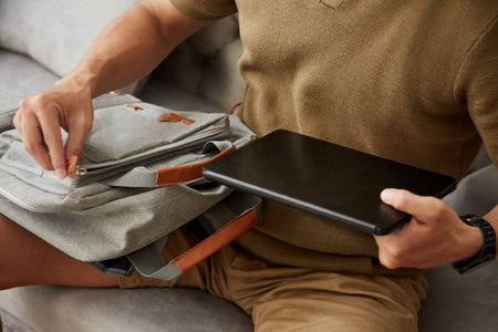 University student putting tablet computer in backpack when leaving house