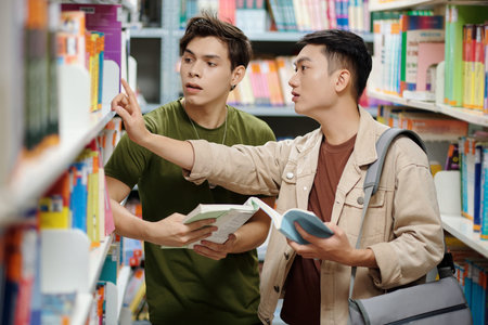 Teenage boy helping classmate to find book in library